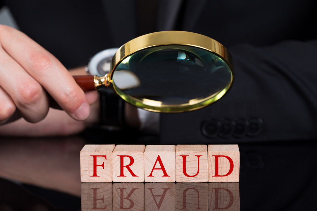 Someone holding a magnifying glass over Fraud wood blocks