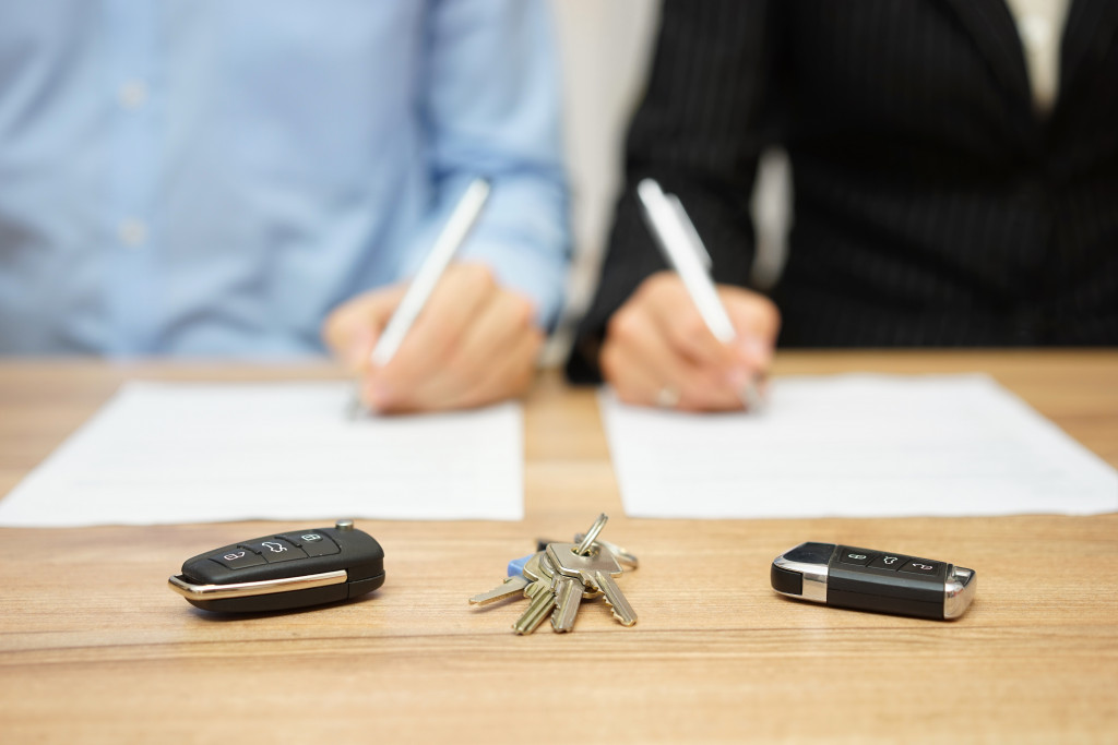 a man and woman signing a paper with house and car keys in focus