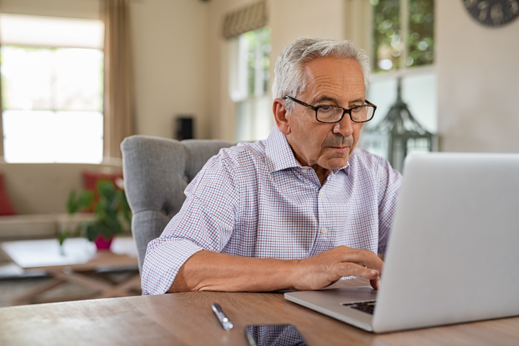 Old man using computer at home sitting on chair 